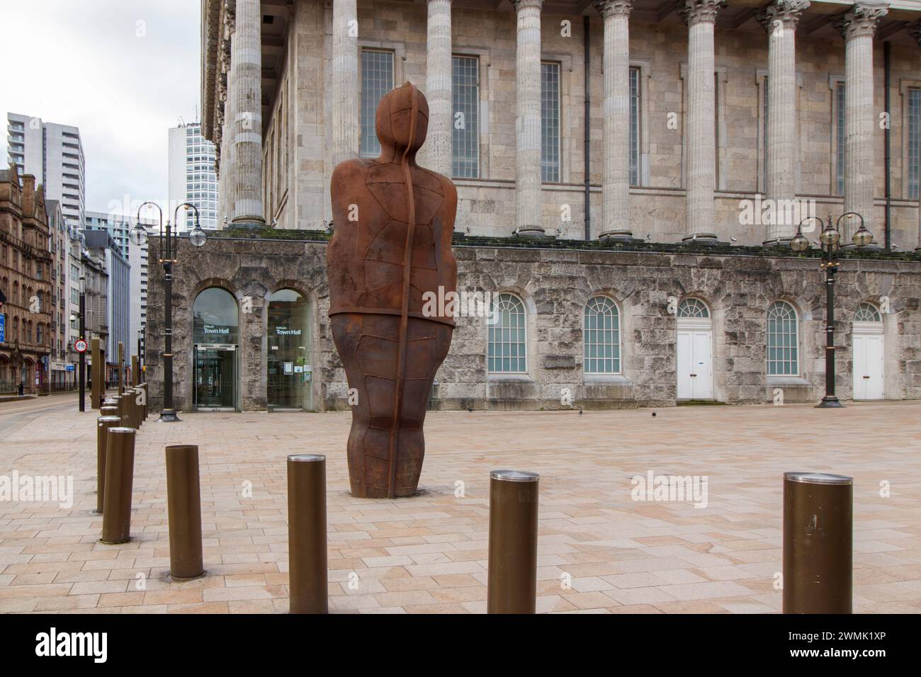 Le Iron Man. La statue a été réinstallée dans un nouvel endroit en 2022 et déplacée après les travaux d'installation d'un nouveau système de tramway à Victoria Square. Iron:Man est une statue d'Antony Gormley, à Victoria Square, Birmingham, en Angleterre. La statue mesure 6 mètres (20 pieds) de haut, y compris les pieds qui sont enterrés sous le trottoir, et pèse 6 tonnes métriques (6 longues tonnes). La statue s'incline à 7,5° vers l'arrière et à 5° vers sa gauche.[1] le sculpteur dit qu'elle représente les compétences traditionnelles de Birmingham et du pays noir pratiquées pendant la révolution industrielle. Birmingham Town Hall peut être vu Banque D'Images