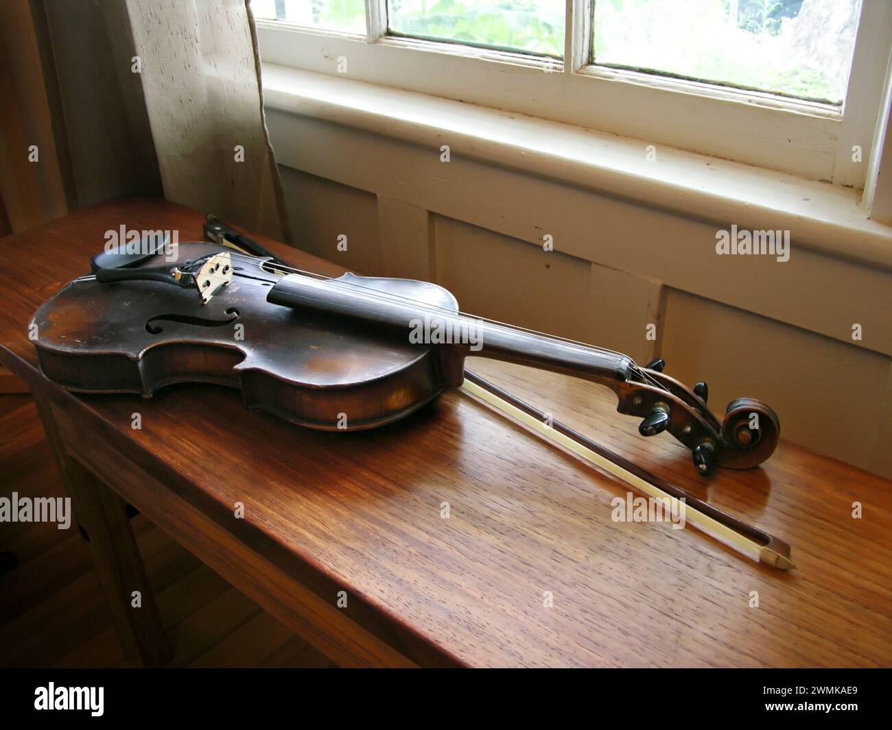 Le violon antique et l'arc reposent sur un banc en bois éclairé par la lumière de la fenêtre Banque D'Images