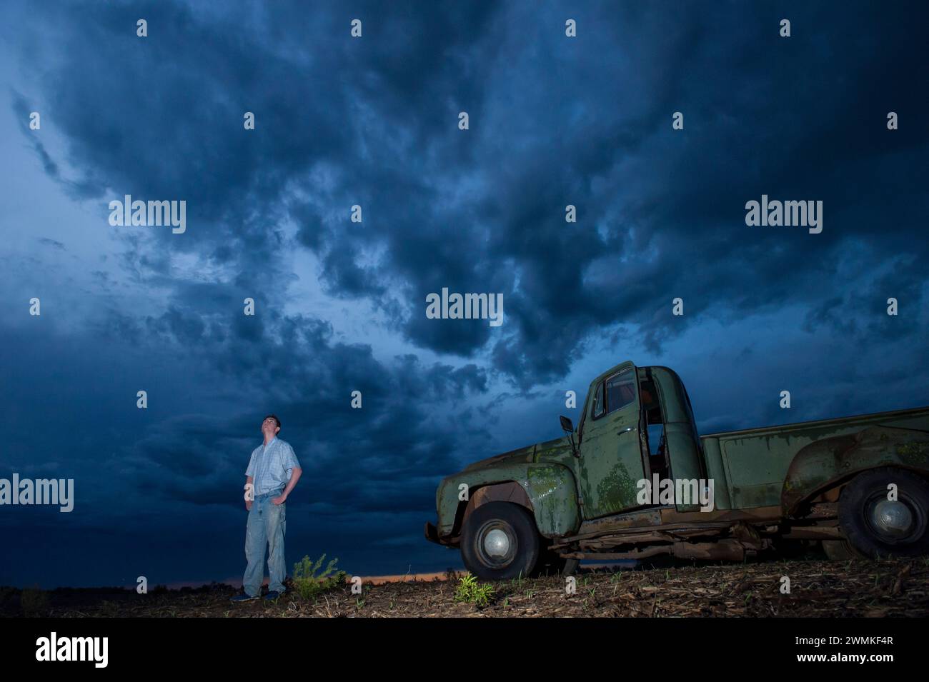 Le jeune homme regarde les nuages de tempête qui se rassemblent dans le ciel près d'un pick-up International Harvester 1951 sur un champ agricole Banque D'Images