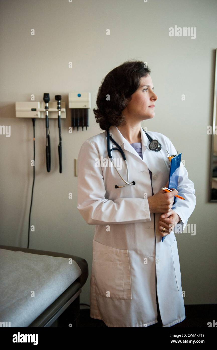L'assistant du médecin tient une planchette à pince tout en regardant par la fenêtre d'une chambre de patient vide ; Lincoln, Nebraska, États-Unis d'Amérique Banque D'Images
