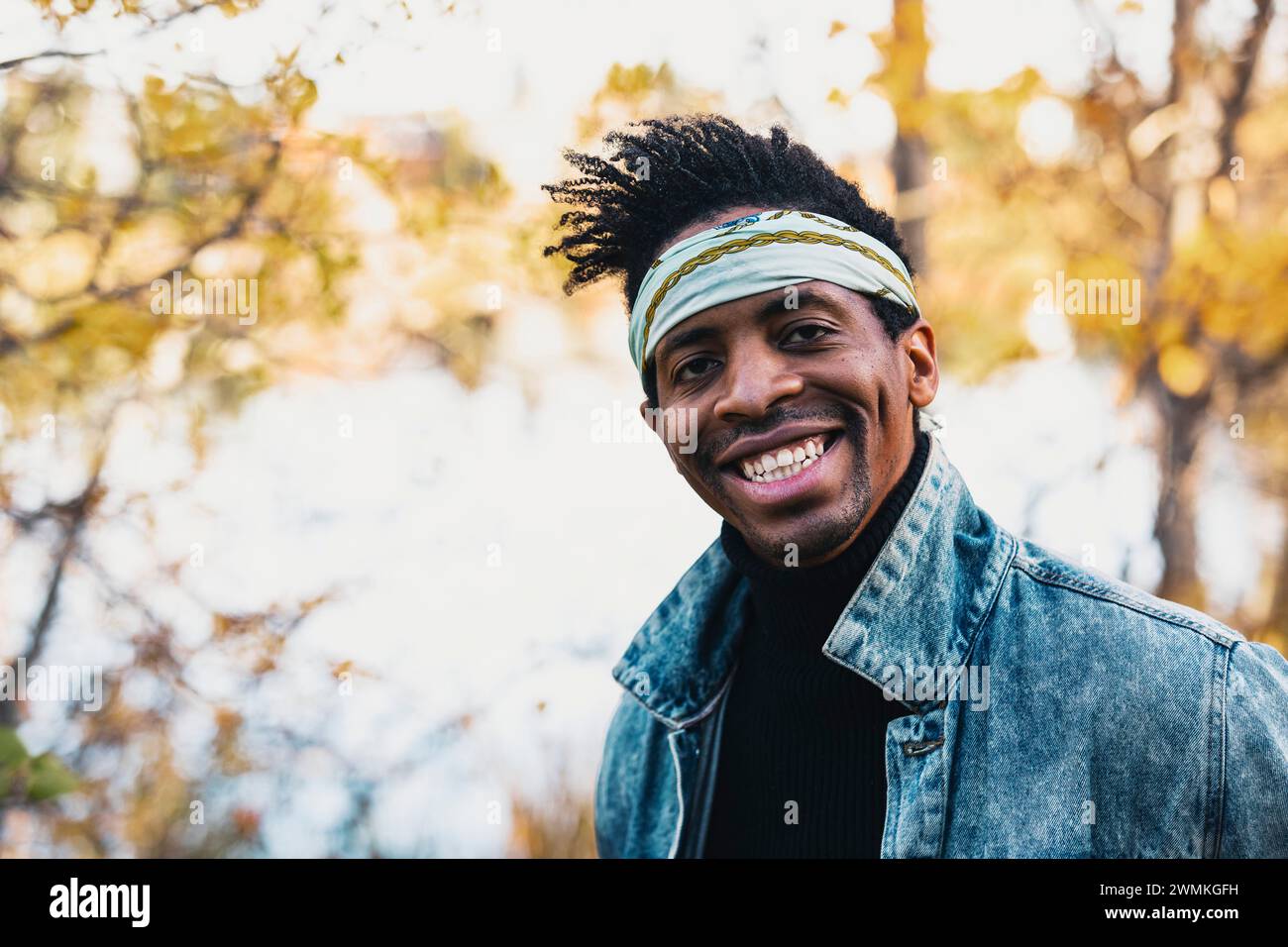 Portrait en gros plan d'un bel homme portant un bandeau bandana, souriant à la caméra dans un parc de la ville à l'automne ; Edmonton, Alberta, Canada Banque D'Images