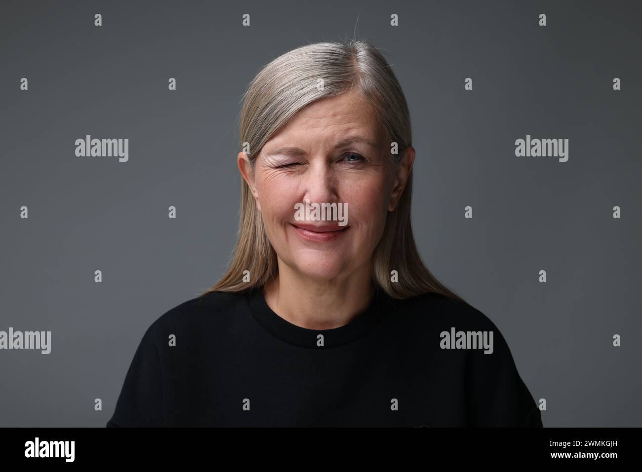 Concept de personnalité. Portrait de femme faisant un clin d'œil sur fond gris Banque D'Images