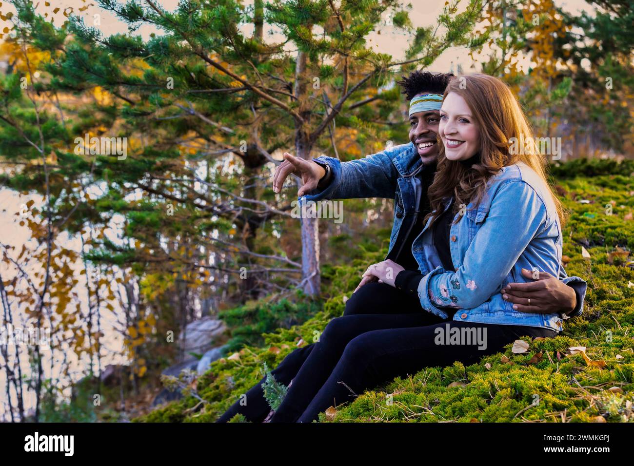 Portrait d'un couple de races mixtes assis sur une colline herbeuse profitant de la vue, passer du temps de qualité ensemble lors d'une sortie en famille d'automne dans une ville... Banque D'Images
