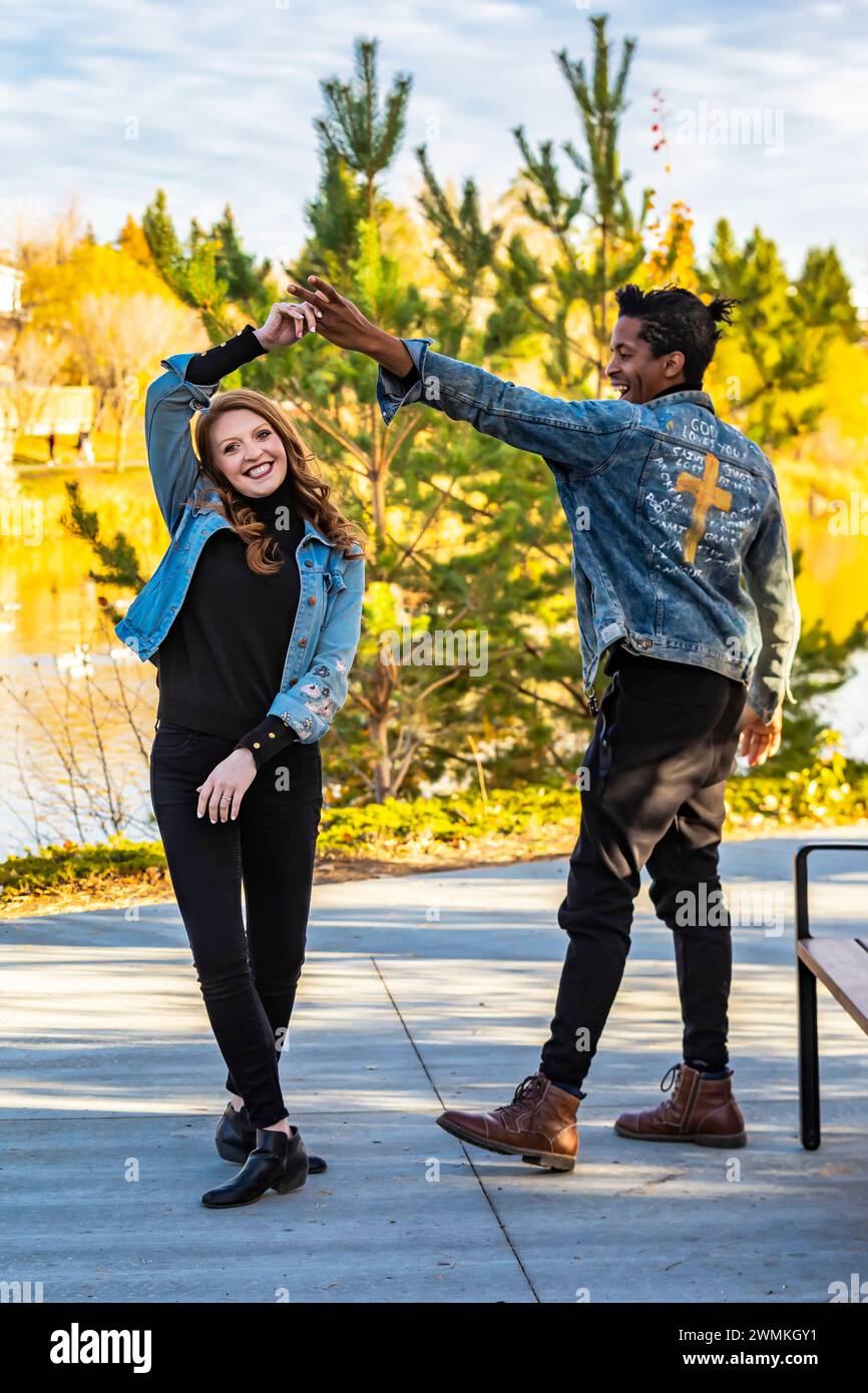 Un couple de courses mixtes dansant et s'amusant tout en passant du temps de qualité ensemble lors d'une sortie en famille d'automne dans un parc de la ville ; Edmonton, Alberta, Canada Banque D'Images