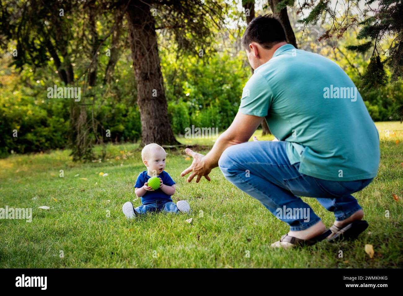 Père passant du temps de qualité et lançant une balle avec son jeune fils atteint du syndrome de Down, dans un parc de la ville pendant un chaud après-midi d'automne Banque D'Images