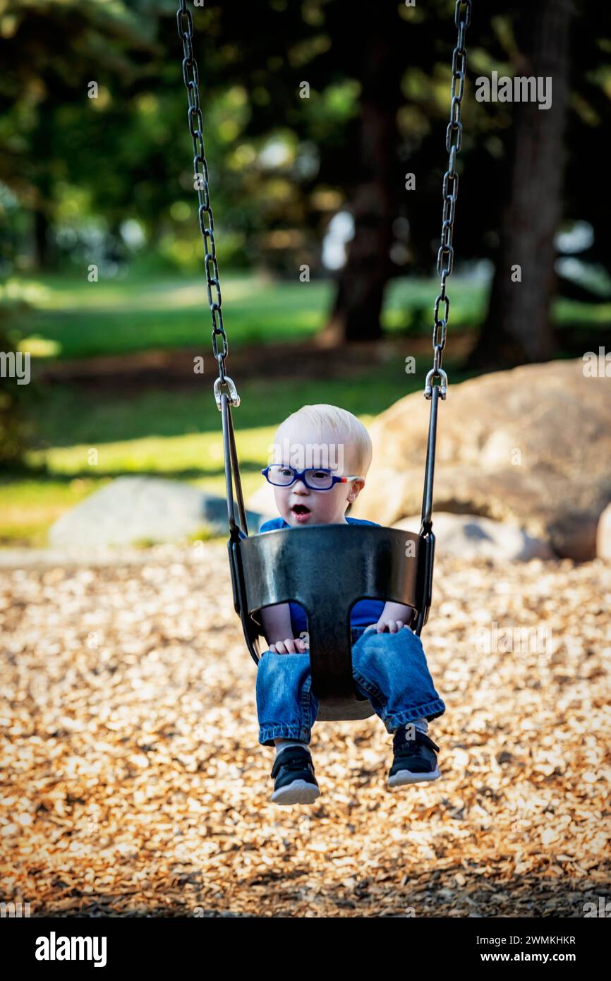 Jeune garçon avec le syndrome de Down balançant dans un parc de la ville, pendant un chaud après-midi d'automne ; Leduc, Alberta, Canada Banque D'Images