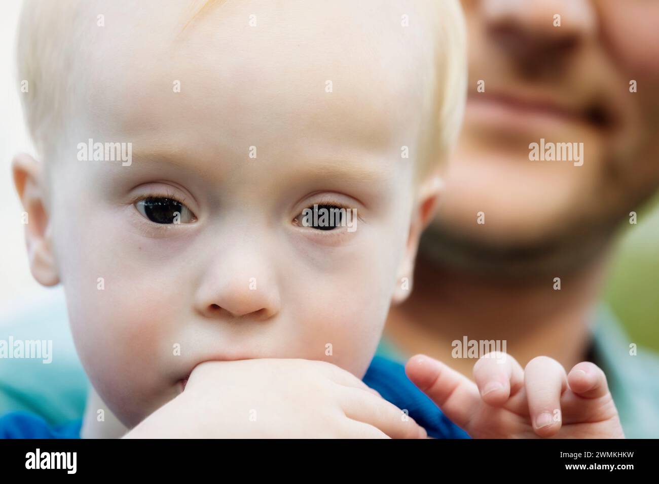 Portrait en gros plan d'un jeune garçon atteint du syndrome de Down, avec son père à l'arrière-plan ; Leduc, Alberta, Canada Banque D'Images