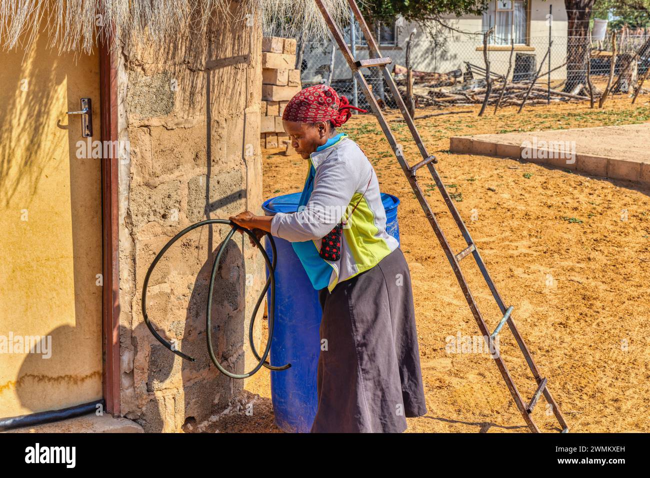 village vieille femme africaine avec un tuyau remplissant les fûts d'eau à côté de sa maison, pour améliorer la vie dans les zones rurales Banque D'Images