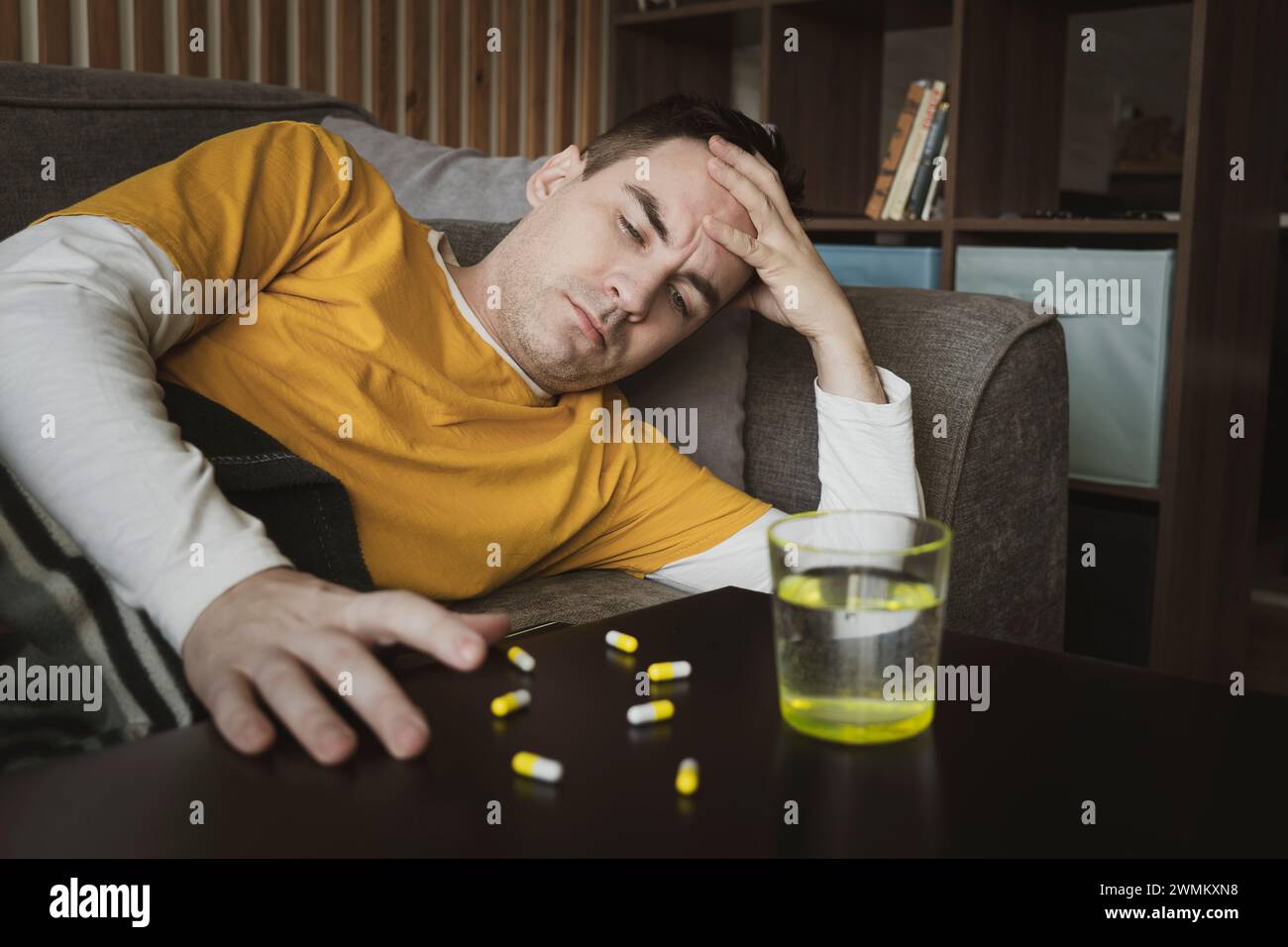 Concept de traitement infection virale à domicile, coronavirus, covid-19 ou grippe, table avec médicaments, pilules, eau, dans la chambre et homme malade défocalisé sur saf Banque D'Images