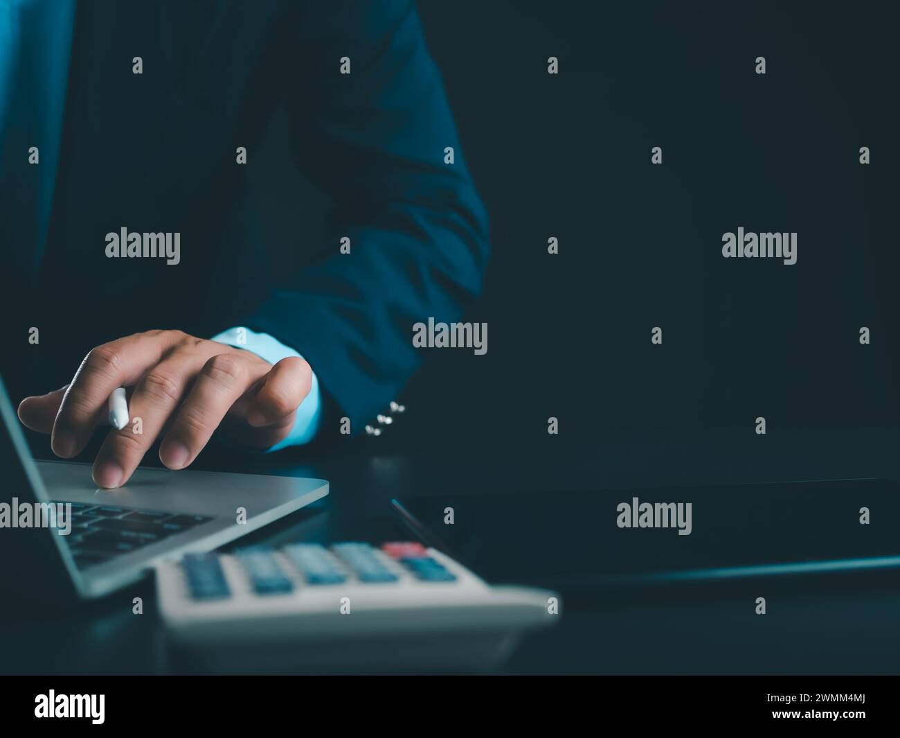 Homme d'affaires en costume noir travaillant sur ordinateur portable et tablette et calculatrice, mains toucher sur tablette au bureau avec fond sombre, travail en ligne Banque D'Images