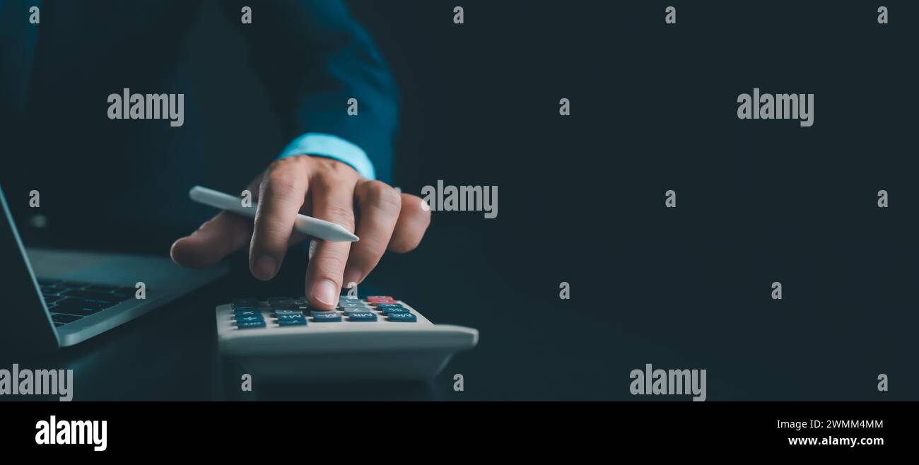 Homme d'affaires en costume noir travaillant sur ordinateur portable et tablette et calculatrice, mains toucher sur tablette au bureau avec fond sombre, travail en ligne Banque D'Images