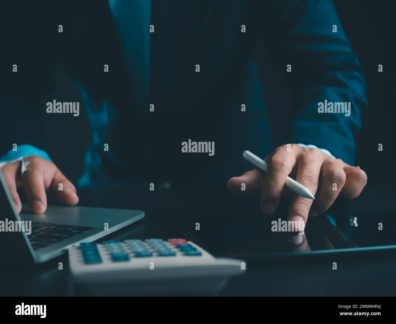 Homme d'affaires en costume noir travaillant sur ordinateur portable et tablette et calculatrice, mains toucher sur tablette au bureau avec fond sombre, travail en ligne Banque D'Images