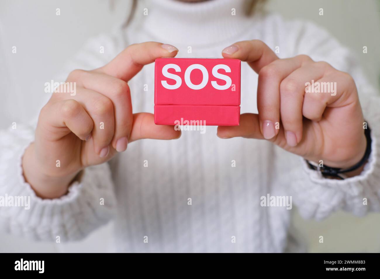 Mains tenant soigneusement une boîte rouge vif étiquetée SOS, symbolisant une aide rapide pour les problèmes de peau Banque D'Images