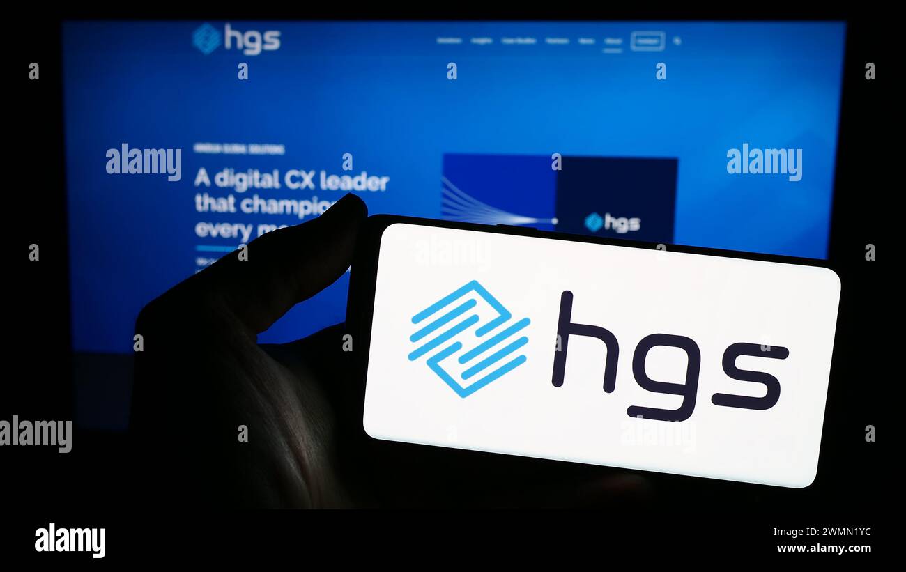 Personne tenant un smartphone avec le logo de la société indienne Hinduja Global solutions Limited (HGS) en face du site Web. Concentrez-vous sur l'affichage du téléphone. Banque D'Images