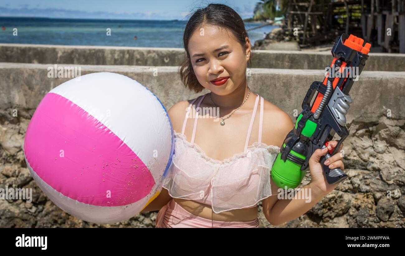 Une fille philippine avec un ballon de plage et un pistolet à eau Banque D'Images