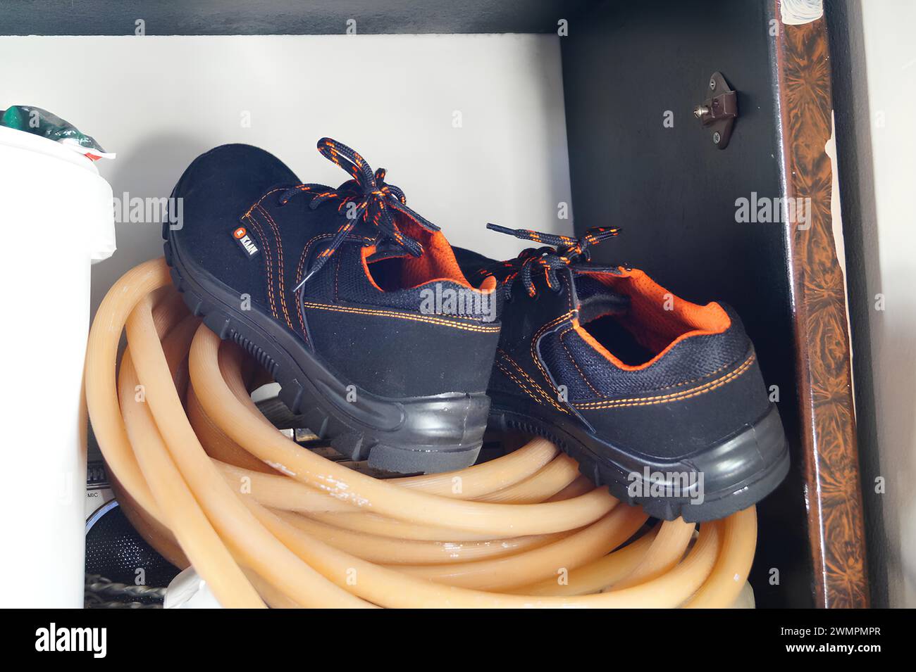 Paire de bottes reposant sur un tuyau orange enroulé à l'intérieur d'une armoire Banque D'Images