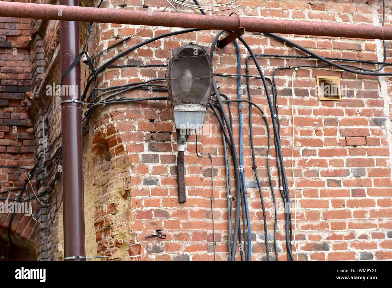 Une lanterne vide oubliée et plusieurs fils électriques accrochent à un vieux mur de pierre. Banque D'Images