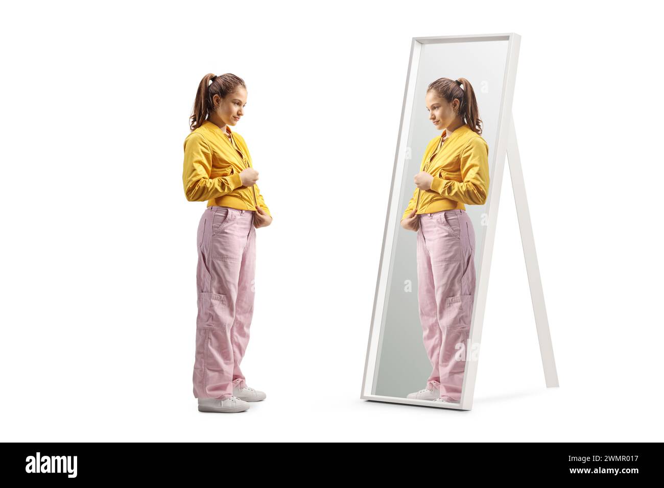 Plan complet d'une adolescente zippant sa veste d'aviateur devant un miroir isolé sur fond blanc Banque D'Images