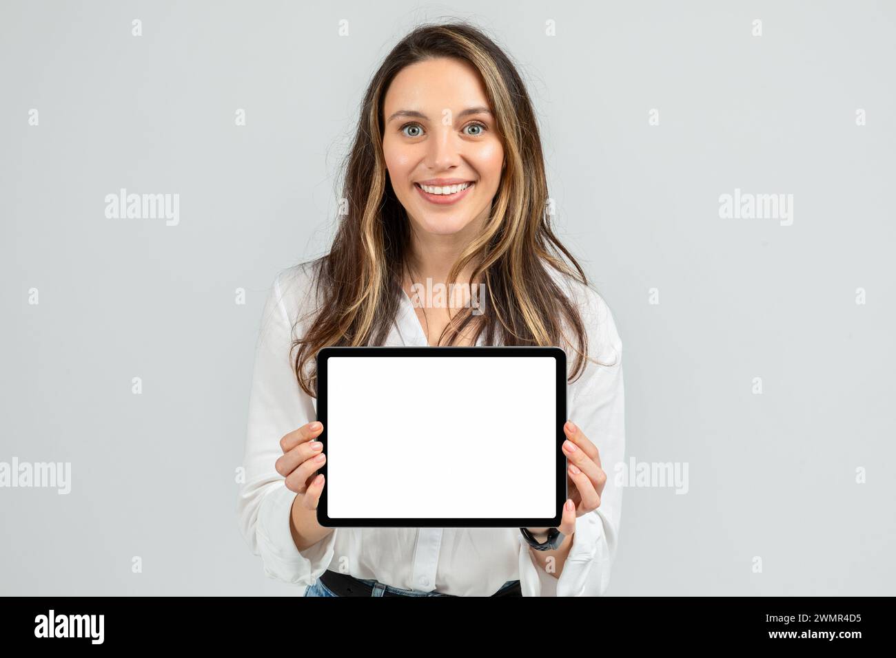 Jeune femme enthousiaste tenant une tablette avec un écran vierge, portant un chemisier blanc et un Jean Banque D'Images