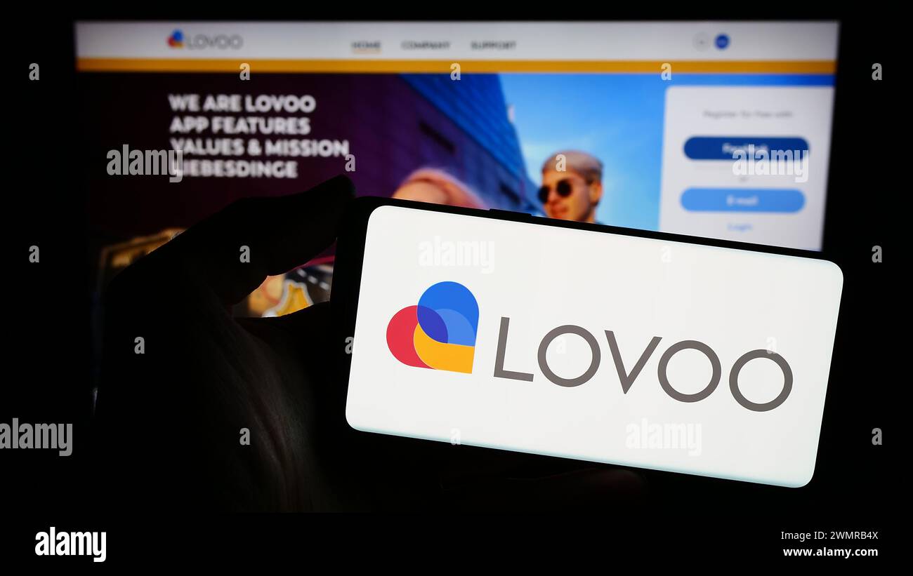 Personne tenant un smartphone avec le logo de la société allemande de plate-forme de rencontres en ligne LOVOO en face du site Web. Concentrez-vous sur l'affichage du téléphone. Banque D'Images