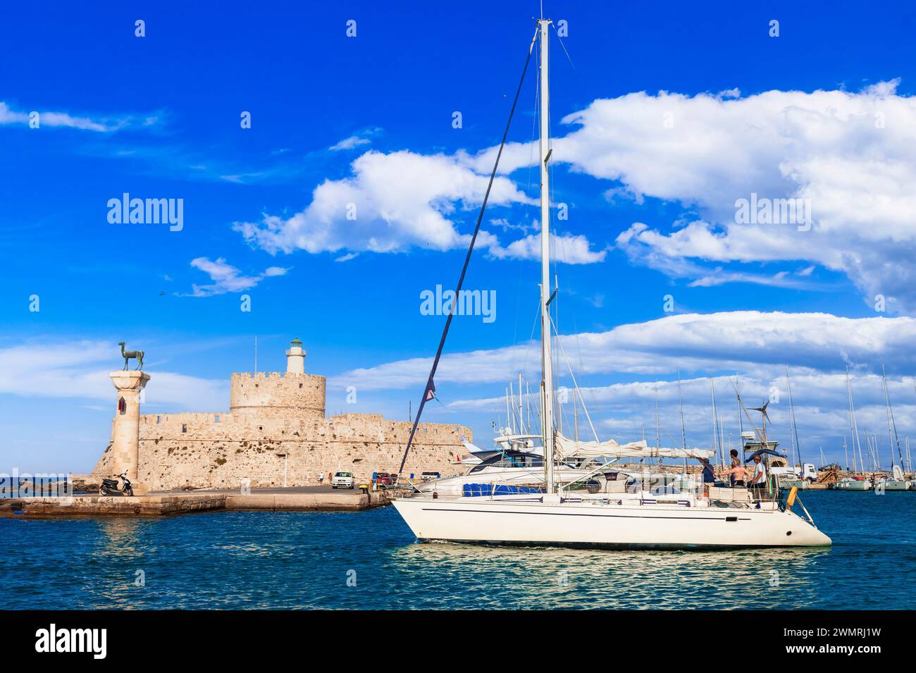 Voyage Grèce, Dodécanèse. Rhodes Island. Port Mandraki avec statue symbole de cerf , saillboats et vieux phare Banque D'Images