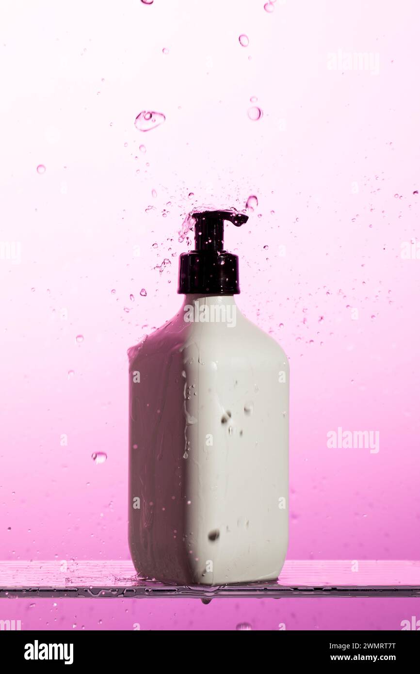 Une bouteille en plastique blanc avec une pompe noire est à flot dans un liquide rose Banque D'Images