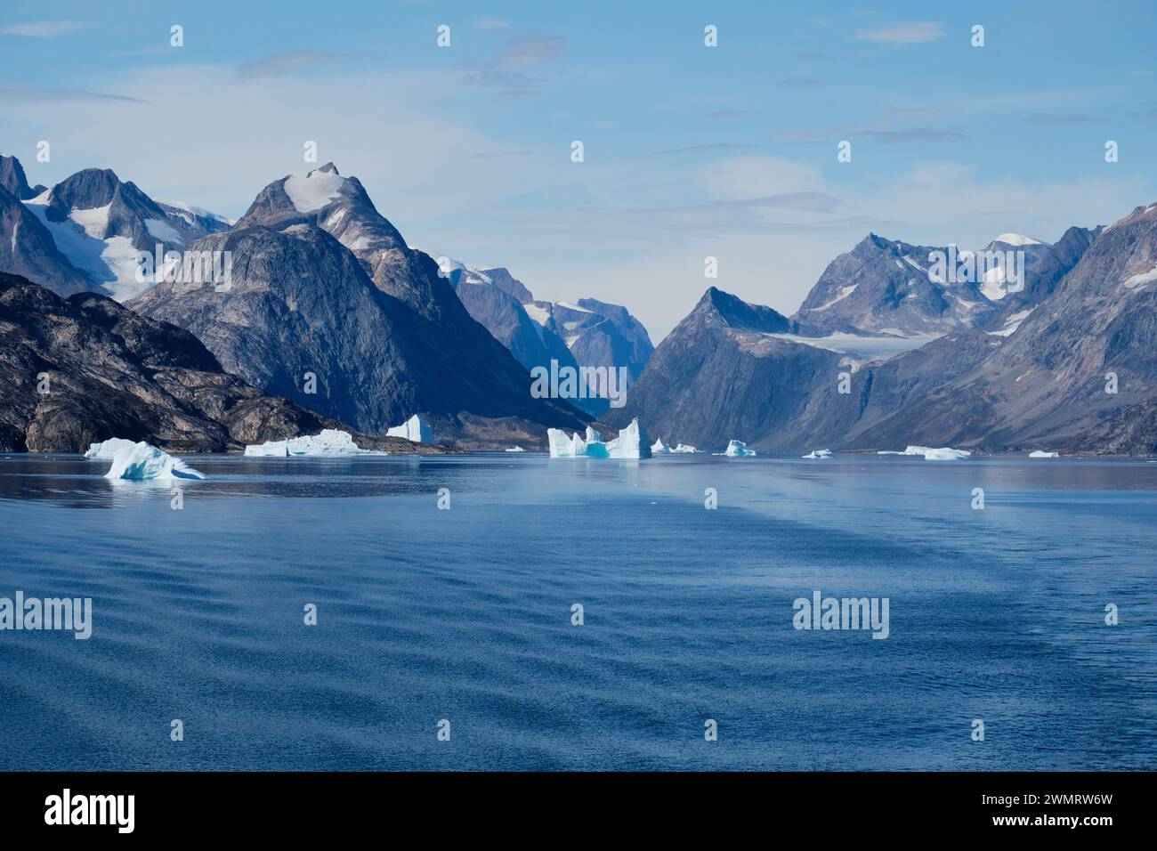 Les montagnes déchiquetées et glaciaires de l'est du Groenland sont entourées d'icebergs et d'une mer bleue brillante Banque D'Images