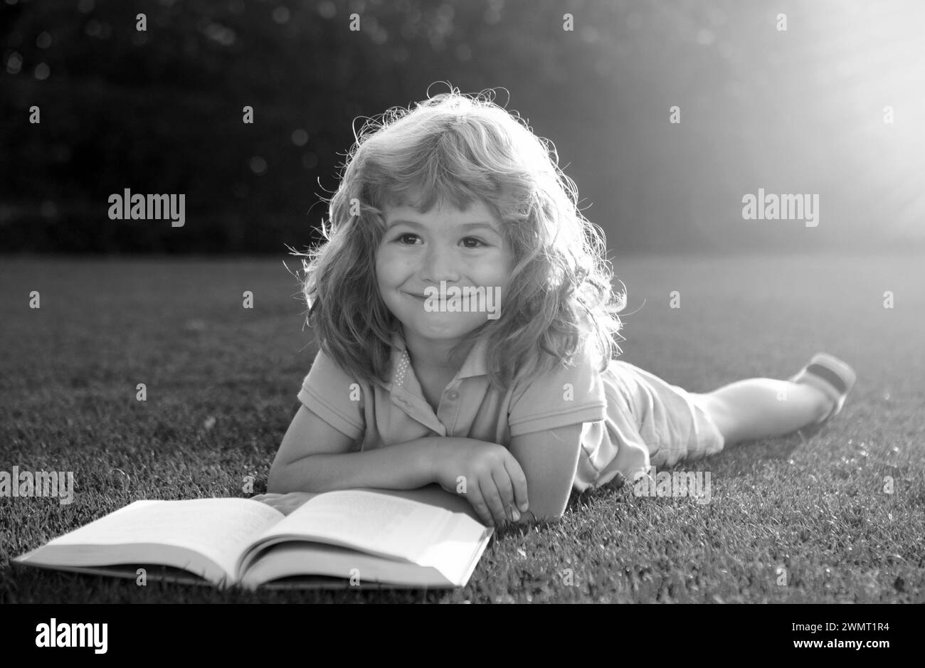 Enfants intelligents.Mignon garçon lisant un livre sur l'herbe.Un enfant lit un livre dans le parc d'été. Banque D'Images