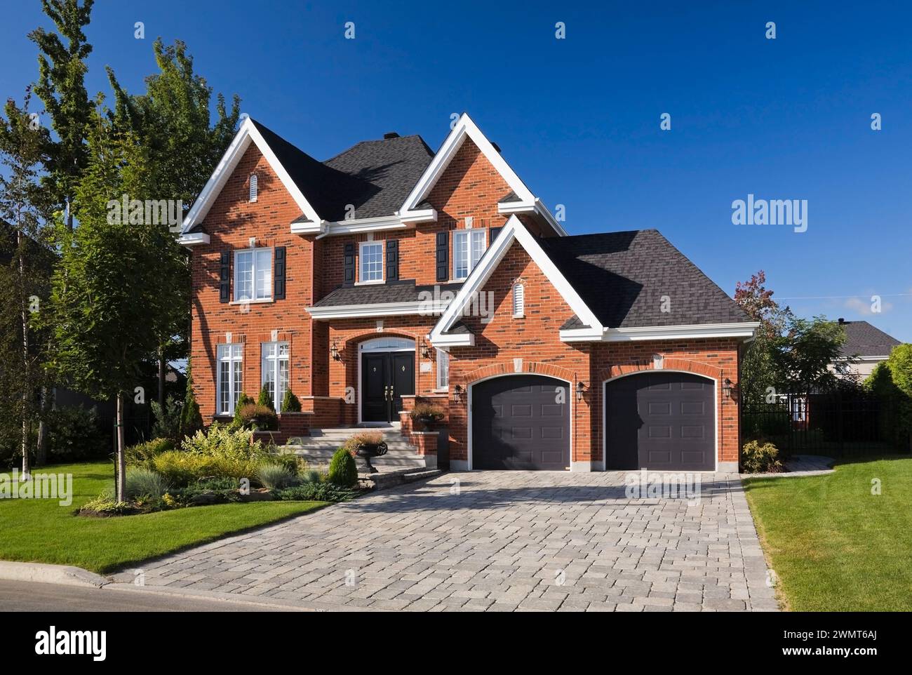 Maison haut de gamme de deux étages en briques rouges et noires avec garage pour deux voitures, allée en pierre pavée et cour avant paysagée en été. Banque D'Images