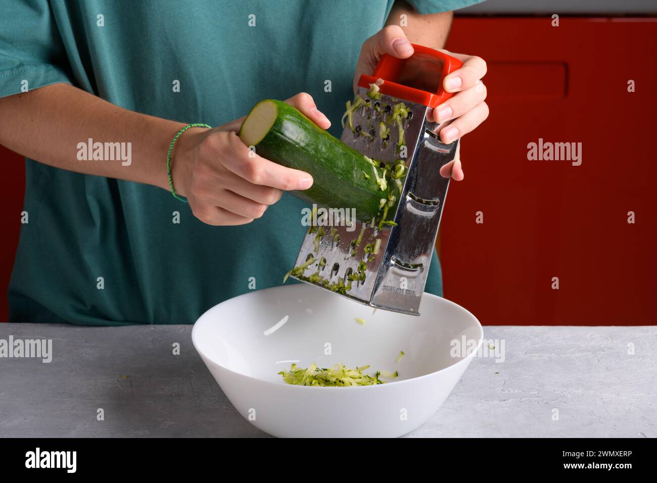 Mains féminines authentiques râpant des courgettes vertes avec une râpe à main en acier inoxydable dans un bol blanc sur la table de cuisine, gros plan, style de vie alimentaire, végétalien et Banque D'Images