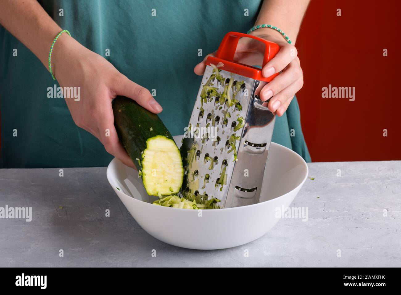 Mains féminines authentiques râpant des courgettes vertes avec une râpe à main en acier inoxydable dans un bol blanc sur la table de cuisine, gros plan, style de vie alimentaire, végétalien et Banque D'Images