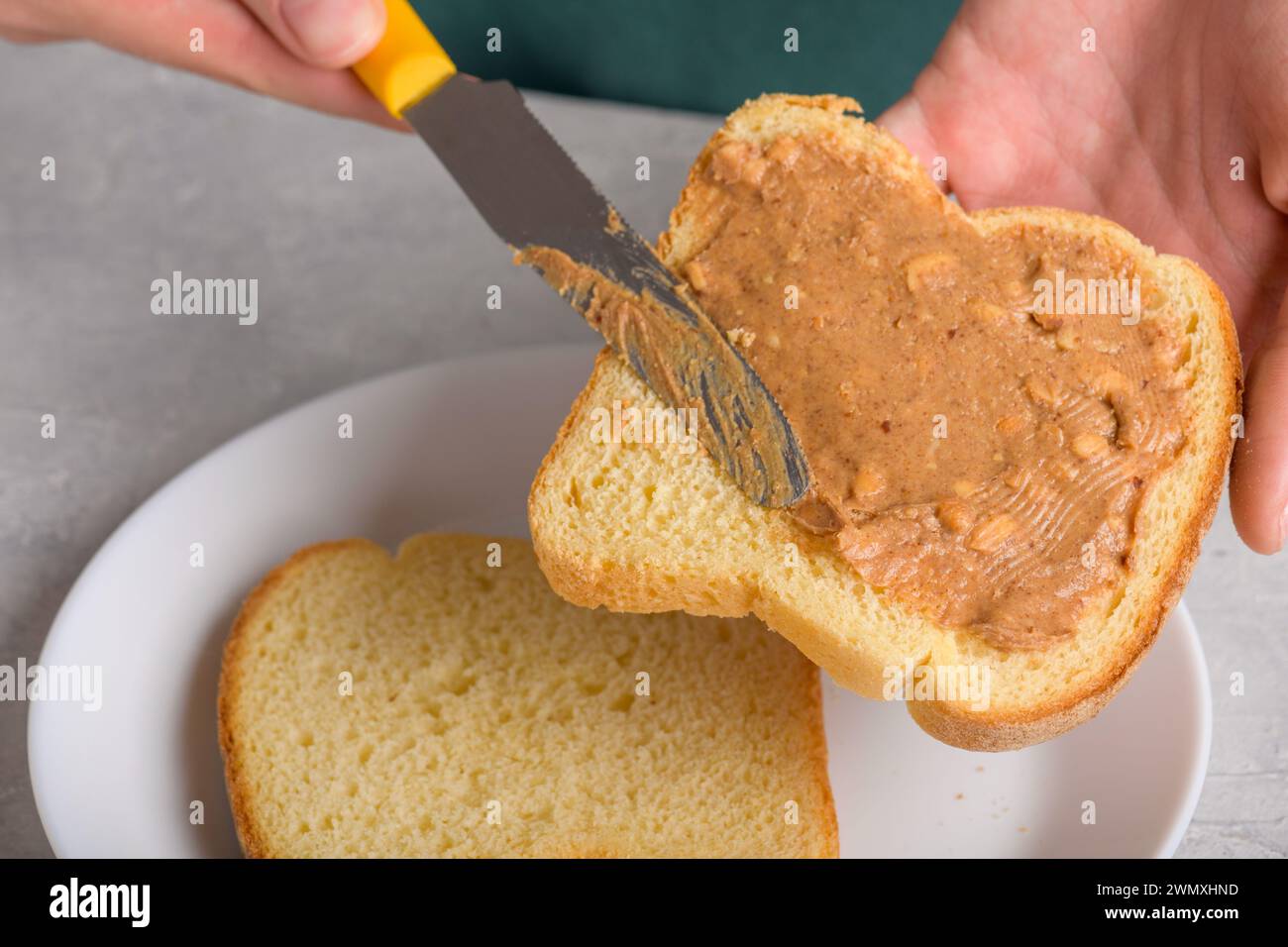 Gros plan de pain blanc toast avec étalement de beurre d'arachide et couteau, les mains de la femme étalent le beurre d'arachide, gros plan, snack typique, style de vie, dom Banque D'Images