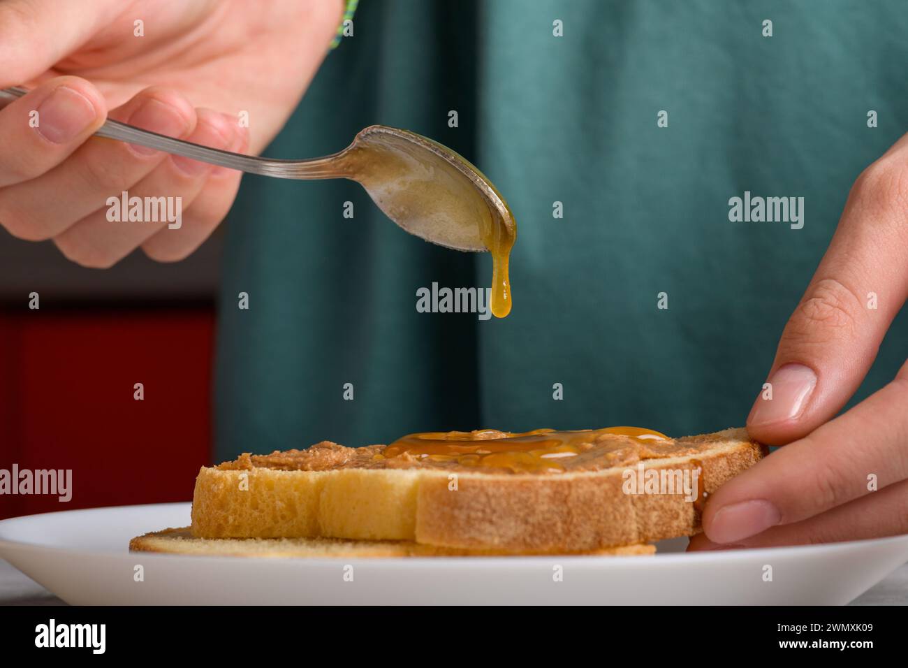 une goutte de miel coulant d'une cuillère sur un sandwich au beurre d'arachide. Les mains de la femme puant le miel avec une cuillère sur un toast avec du beurre d'arachide pour faire un s. Banque D'Images