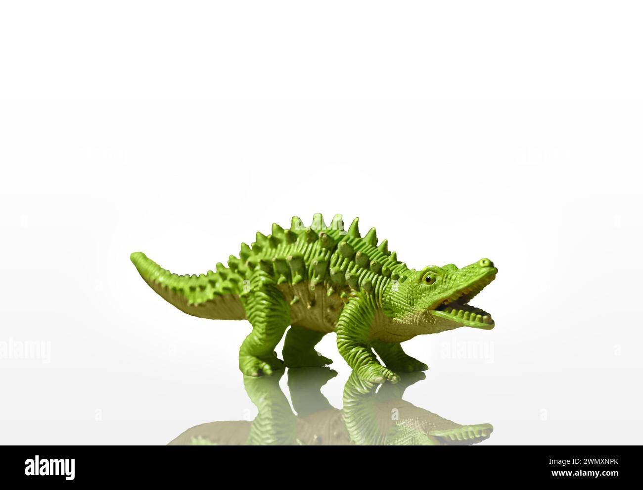 Figurine d'un dinosaure vert avec des pointes isolé sur un fond blanc avec reflet ajouté Banque D'Images