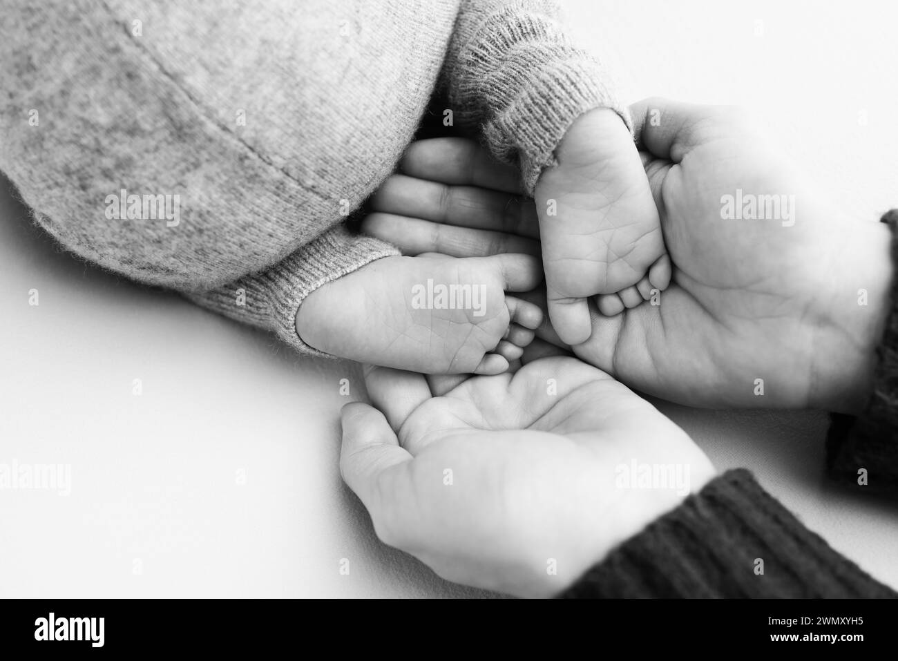 Les pieds du nouveau-né sur les paumes des parents. Studio macro photo noir et blanc des orteils, talons et pieds d'un enfant. Banque D'Images