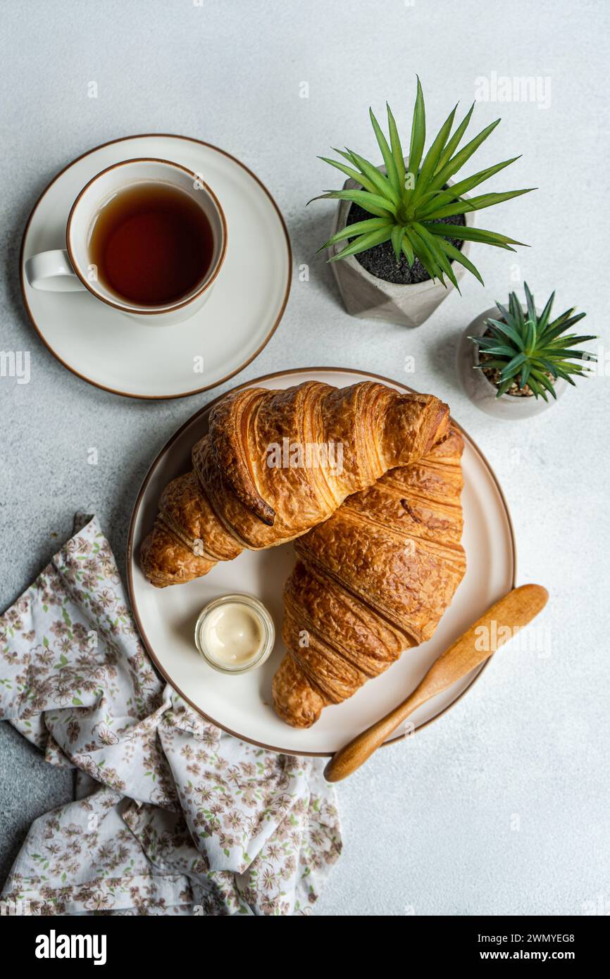 Vue de dessus d'une scène de petit déjeuner avec des croissants feuilletés, un pot de miel, une tasse de thé et des succulentes décoratives en pot sur une surface texturée Banque D'Images