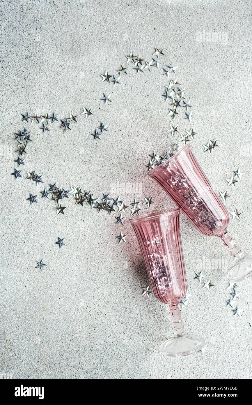 Du haut de deux verres à champagne roses posés avec une traînée de confettis argentés en forme d'étoile sur une surface blanche texturée Banque D'Images