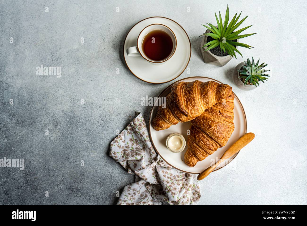Vue de dessus d'une scène de petit déjeuner avec des croissants feuilletés, un pot de miel, une tasse de thé et des succulentes décoratives en pot sur une surface texturée Banque D'Images