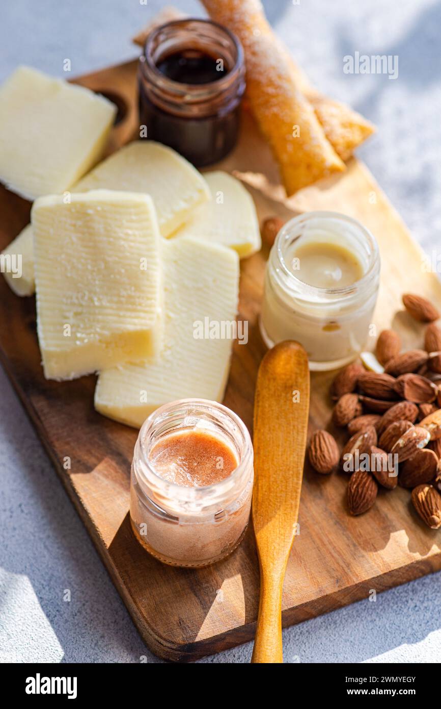 Une sélection de fromages gourmands sur une planche de bois, associée au miel, aux noix et aux délicieuses pâtes à tartiner, parfaite pour les collations élégantes ou les divertissements Banque D'Images