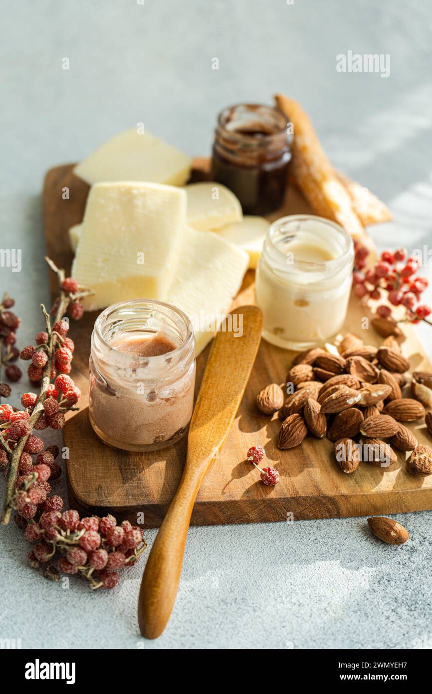Une planche de fromage rustique avec des tranches de fromage artisanal, des amandes, des baies rouges et des pots de miel, avec un étaleur sur le côté Banque D'Images