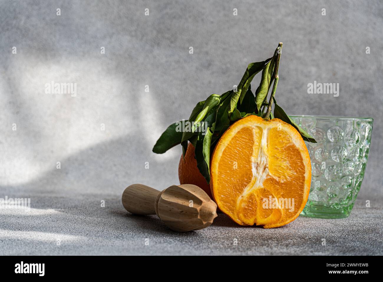 Une image séduisante capturant un orange coupé en deux avec une centrifugeuse en bois et un verre vide, le tout sur un fond gris texturé, évoquant un et naturel Banque D'Images