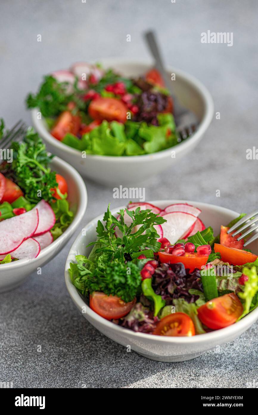 Salade de légumes fraîchement préparée avec laitue croustillante, roquette, radis tranchés, tomates cerises, oignons verts, et des graines de grenade dans un bo blanc Banque D'Images