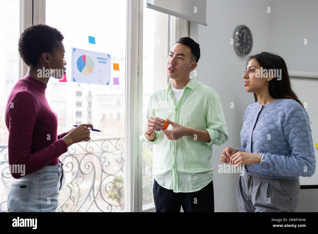 Trois professionnels s’engagent dans une discussion stratégique avec une planche de verre dans un bureau bien éclairé Banque D'Images