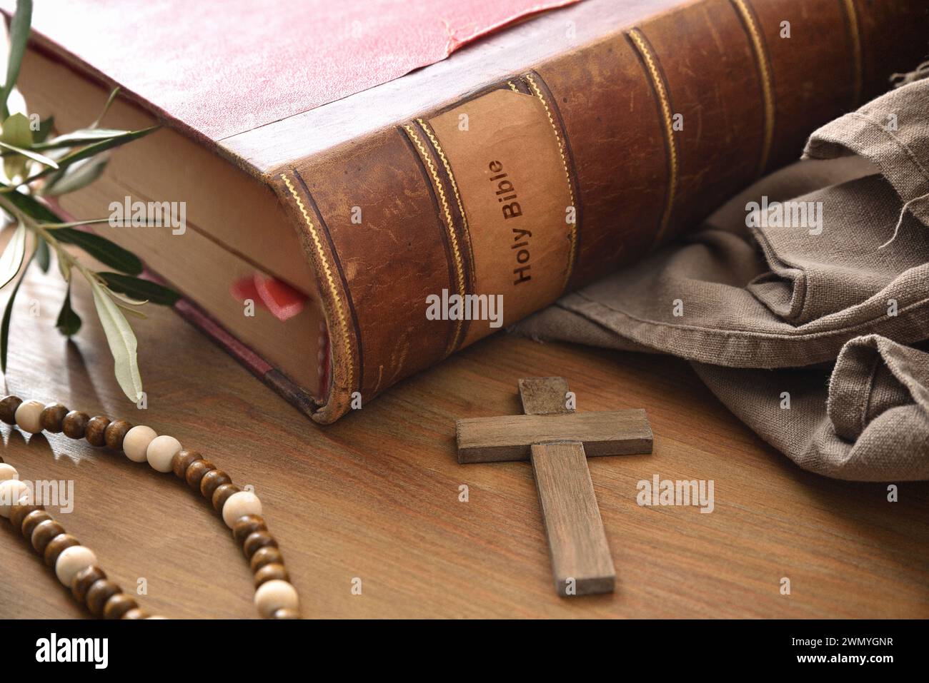 Bible antique sur table en bois avec croix chrétienne en bois, feuilles d'olivier et tissu brun. Vue surélevée. Banque D'Images