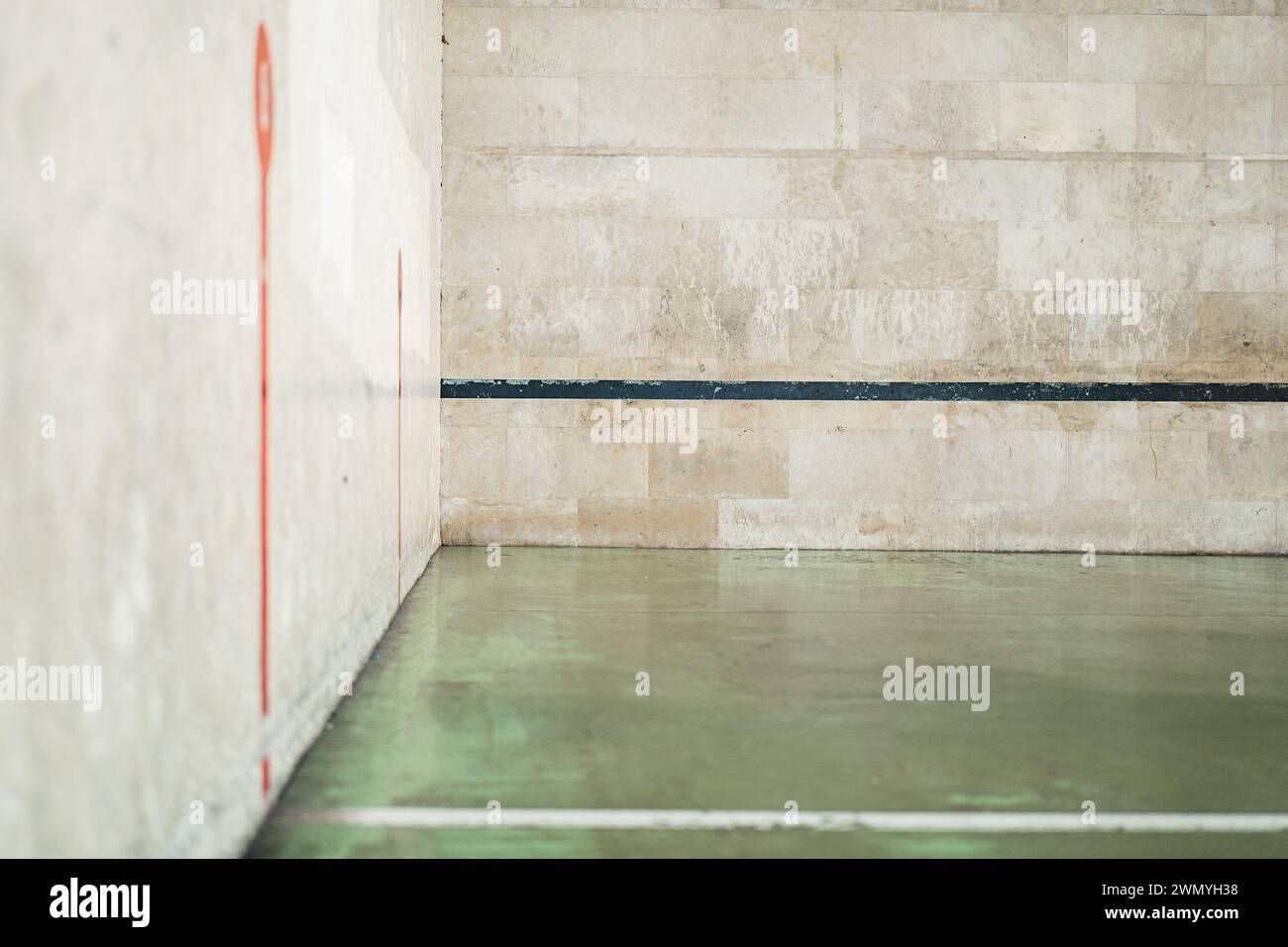 Une vue d'un terrain de handball extérieur vide avec des lignes rouges distinctives sur un mur de béton et une ligne noire sur le sol, montrant des signes d'usure Banque D'Images
