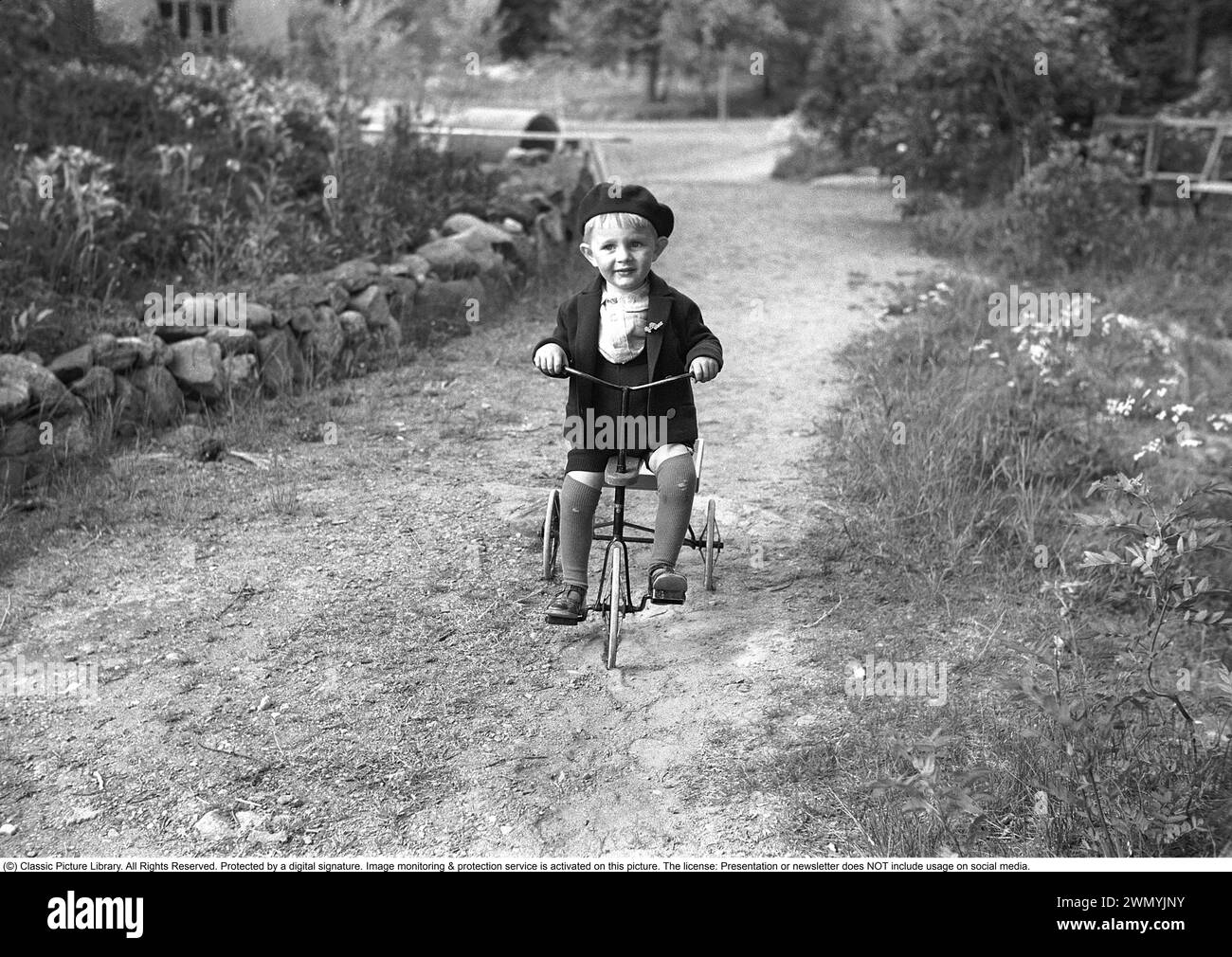 enfant des années 1930. Un petit enfant est sur son tricycle. Charmante photo du garçon vêtu d'une veste et d'un béret. Les chaussettes longues sont portées avec des trous sur les genoux. 1939. Photo Kristoffersson 155-5 Banque D'Images