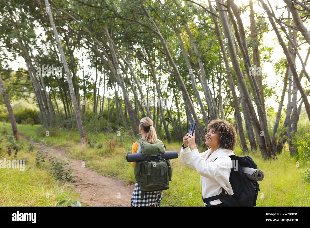 Deux femmes font une randonnée en forêt, dont l'une capture le paysage avec son appareil photo Banque D'Images