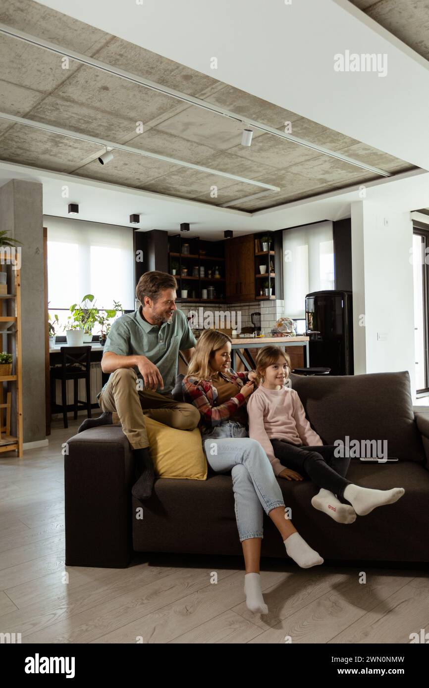 La famille profite d'un moment de détente ensemble sur le canapé, avec des interactions ludiques et des sourires chaleureux Banque D'Images