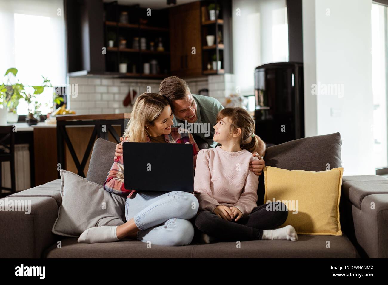 Joyeuse famille de trois passe du temps de qualité ensemble sur le canapé du salon, partageant un moment autour d'un ordinateur portable dans leur maison confortable Banque D'Images