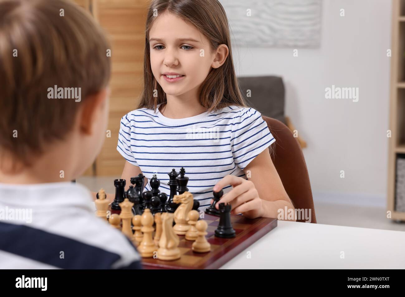 Enfants mignons jouant aux échecs à table dans la chambre Banque D'Images